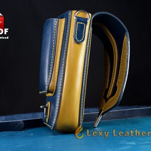 May include: A blue and yellow leather crossbody bag with a strap and a small pocket on the front. The bag has yellow stitching and a silver buckle.