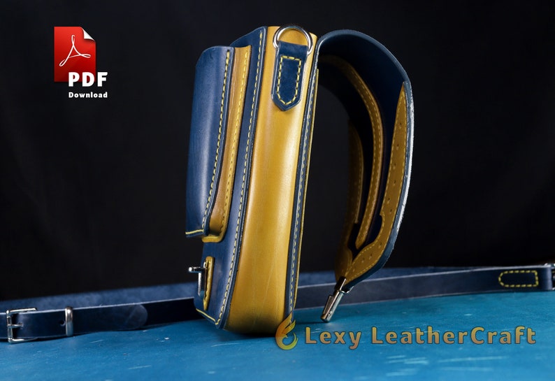 May include: A blue and yellow leather crossbody bag with a strap and a small pocket on the front. The bag has yellow stitching and a silver buckle.