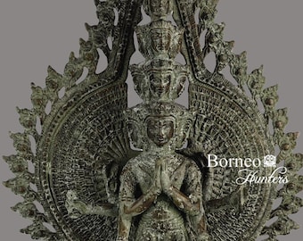 May include: A green bronze statue of a multi-armed deity with a crown and a halo. The deity is standing on a base with intricate carvings. The statue is surrounded by a circular design of leaves and flowers.
