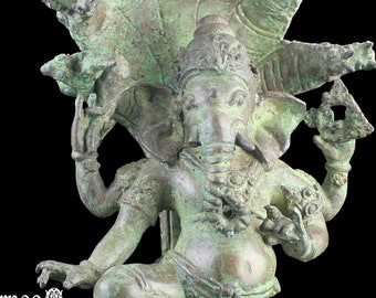 Op de afbeelding: Een groene bronzen beeld van Ganesha, de hindoeïstische god van wijsheid en voorspoed, staand op een slang. Hij heeft vier armen en houdt verschillende voorwerpen vast, waaronder een lotusbloem, een bijl en een kom met snoepjes. Hij draagt een kroon en een bloemenkrans. Het beeld is versierd met ingewikkelde details en is een prachtig voorbeeld van traditionele Indiase kunst.