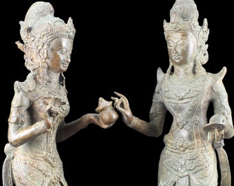 Op de afbeelding: Een paar antieke bronzen beelden van twee figuren, waarschijnlijk godheden, die op zwarte sokkels staan. De figuren zijn ingewikkeld gedetailleerd en hebben een groene patina. De beelden zijn ongeveer 30 cm hoog.