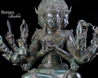 Puede incluir: Una estatua de bronce verde de una deidad con cuatro brazos y tres cabezas. La deidad está sentada en una postura meditativa sobre una base de loto. La estatua está intrincadamente detallada y tiene una pátina desgastada.