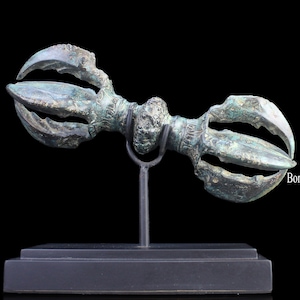 May include: A bronze ceremonial weapon with a double-headed design, featuring intricate details and a green patina. The weapon is mounted on a black stand.