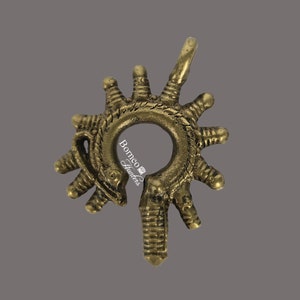 Könnte beinhalten: Ein goldfarbener Metallanhänger mit einem runden Design und einem dekorativen, komplizierten Muster. Der Anhänger hat oben eine Schlaufe zum Aufhängen.