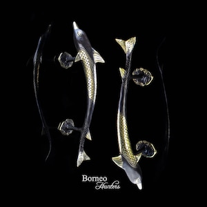 Könnte beinhalten: Zwei schwarze und goldene Delfin-Türgriffe mit filigranen Details. Die Griffe sind aus Metall und haben eine polierte Oberfläche.