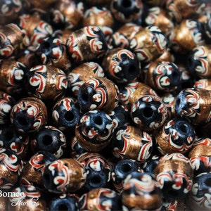 May include: A close-up of a pile of black, white, and gold beads with intricate swirling patterns. The beads are made of glass and have a glossy finish.