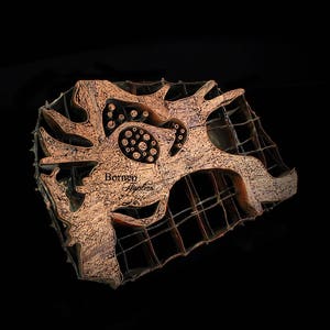 May include: A copper-colored batik stamp with a complex design featuring a central motif of a stylized flower with a grid pattern surrounding it. The stamp is labeled "Borneo Batiks".