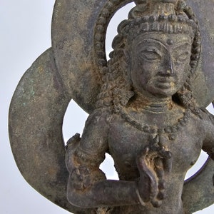 Puede incluir: Una estatua de bronce de una deidad con un halo, de pie en una pose meditativa. La estatua está intrincadamente detallada y tiene una pátina desgastada.