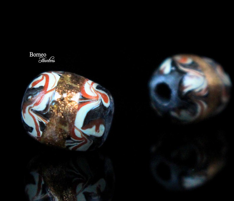 May include: Two colorful glass beads with intricate swirling patterns in shades of red, white, black, and gold. The beads have a slightly irregular shape and a glossy finish.