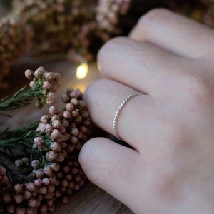 Op de afbeelding: Een delicate zilveren ring met een gedraaid ontwerp. De ring wordt aan een vinger gedragen en is een eenvoudig, minimalistisch sieraad.