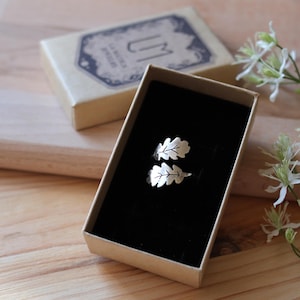 Op de afbeelding: Een zilveren ring met twee eikenbladeren. De ring zit in een klein, bruin doosje met een zwarte binnenkant.