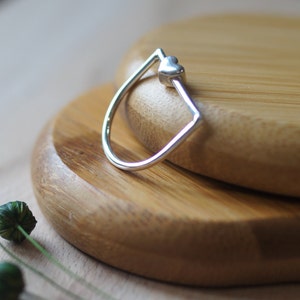 Könnte beinhalten: Ein silberner Ring mit einem herzförmigen Design. Der Ring liegt auf einer Holzoberfläche.