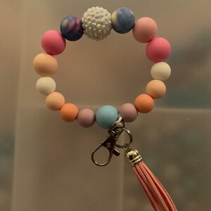 May include: A colourful beaded bracelet with a sparkly charm and a pink tassel keyring.