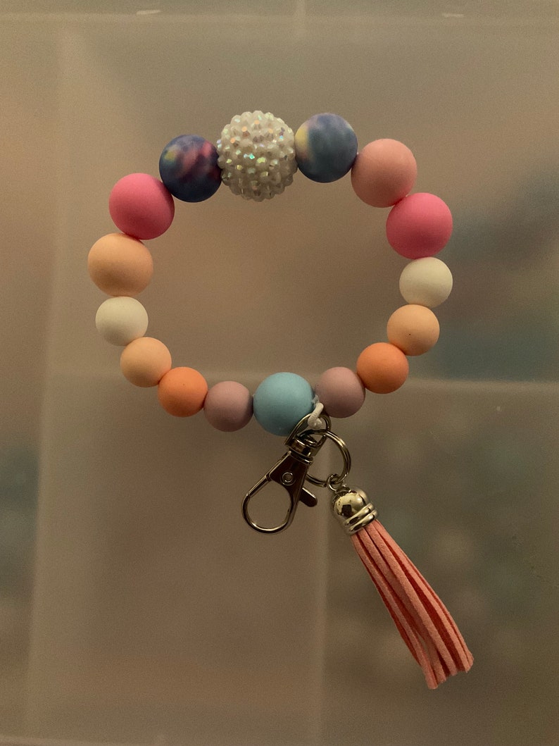 May include: A colourful beaded bracelet with a sparkly charm and a pink tassel keyring.