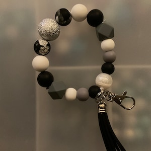 May include: A black and white beaded bracelet with a silver charm and a black tassel keyring.