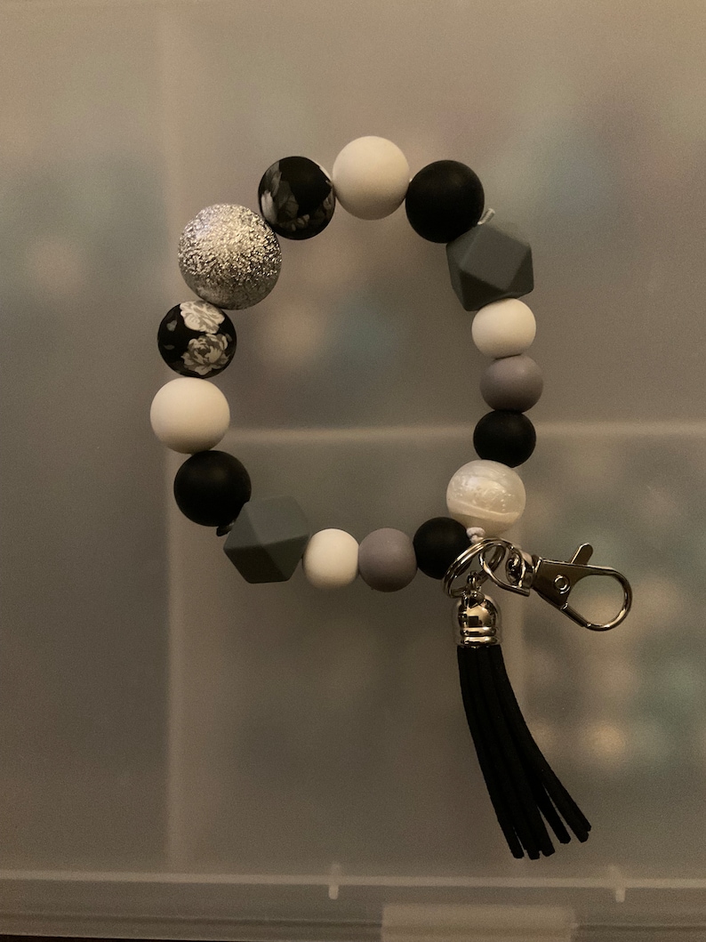 May include: A black and white beaded bracelet with a silver charm and a black tassel keyring.