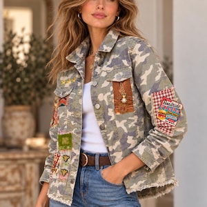 May include: A camouflage print jacket featuring a frayed hem, button-down front, and various decorative patches including a Roadside Diner sign, a bee emblem, and geometric patterns. The jacket is worn over a plain white tank top and blue jeans.