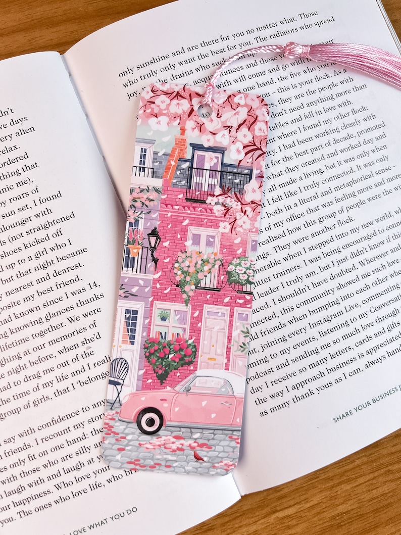 Pode incluir: Marca-p&aacute;ginas rosa e branco com um carro rosa, flores e um pr&eacute;dio rosa com telhado branco. O marca-p&aacute;ginas tem o texto "to".