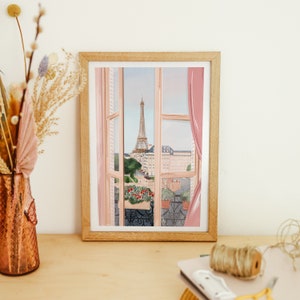 Op de afbeelding: Een ingelijste illustratie van een raam met uitzicht op de Eiffeltoren in de verte. Het raam is open en heeft roze gordijnen. Er staan bloemen op het balkon.