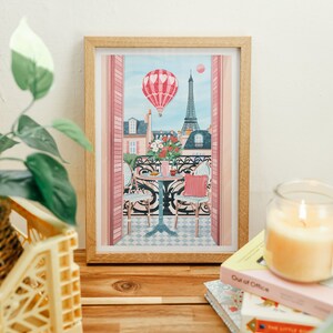 May include: A framed illustration of a Parisian balcony scene with a hot air balloon, Eiffel Tower, and a table with two chairs. The balloon is pink and white with hearts, and the Eiffel Tower is in the background. The balcony is decorated with pink flowers.