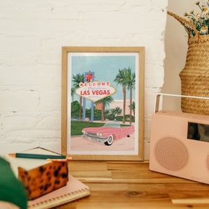 May include: A framed illustration of the iconic "Welcome to Fabulous Las Vegas" sign with a pink vintage car driving in front of it. The illustration is set against a blue sky with palm trees in the background.