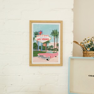 May include: A framed illustration of a pink car driving past the "Welcome to Fabulous Las Vegas, Nevada" sign with palm trees in the background.