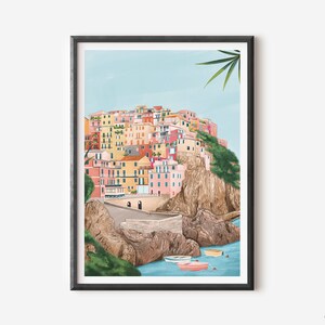 May include: A framed art print depicting a colorful coastal village nestled on a cliffside. The buildings are painted in shades of pink, yellow, and orange, with a light blue sky and turquoise water. Several small boats float in the water below.