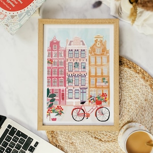 Puede incluir: Una ilustraci&oacute;n enmarcada de edificios coloridos con una bicicleta roja en frente. Los edificios tienen acentos rojos, amarillos y blancos. La bicicleta tiene una cesta con flores.