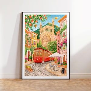 Op de afbeelding: Een ingelijste aquarel schildering toont een Europese straatscène met een rode tram op een geplaveide spoorbaan. Gebouwen in tinten oranje, roze en geel omzomen de straat, met een grote kerk op de achtergrond. Rechts is een café met een witte parasol en een kleine tafel.