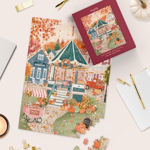 May include: A 500-piece jigsaw puzzle titled Autumn Festival featuring a scene of a town square with a gazebo, pumpkins, a creamery, and a red truck. The puzzle box is deep red, and the assembled puzzle shows a colorful fall landscape.