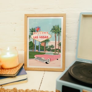 May include: A framed illustration of the "Welcome to Fabulous Las Vegas" sign with a pink vintage car in front of it. The illustration is set against a blue sky with palm trees.