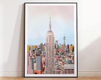 Puede incluir: Una impresión enmarcada de un colorido paisaje urbano, con el Empire State Building como foco central. La obra de arte presenta una vibrante variedad de edificios en tonos rosa, amarillo, naranja y azul, sobre un cielo suave y pastel. El marco es negro.