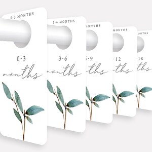 May include: Five white door hangers with a hole at the top for hanging. Each hanger has a different age range printed on it in black text: 0-3 months, 3-6 months, 6-9 months, 9-12 months, and 12-18 months. Each hanger has a watercolor illustration of a green leafy branch.