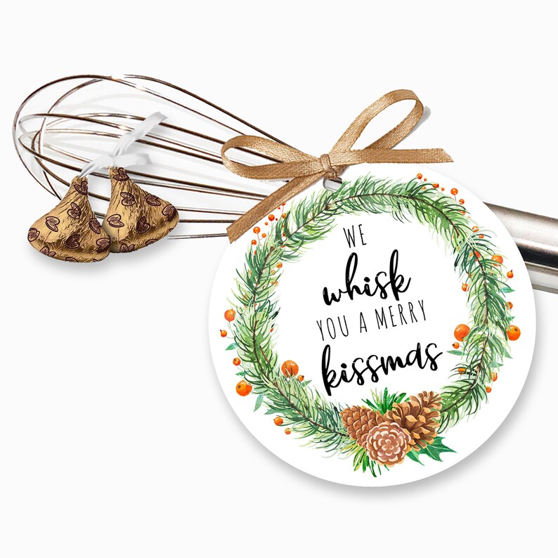 May include: Round white gift tag with a green watercolor wreath, pine cones, and red berries. The text reads "We whisk you a merry kissmas".