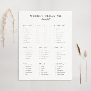 Könnte beinhalten: Ein weißes Papier mit einer gedruckten wöchentlichen Reinigungscheckliste. Die Checkliste umfasst tägliche, wöchentliche und Wochentagsaufgaben. Der Text ist in einer einfachen, eleganten Schriftart gehalten. Getrocknete Blumen sind an der Seite befestigt.