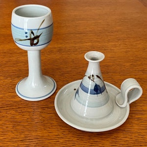 Puede incluir: Un juego de dos candelabros de cerámica con diseños pintados en azul y marrón. El candelabro de la izquierda tiene forma de copa alta, mientras que el candelabro de la derecha es un plato bajo y ancho con asa.