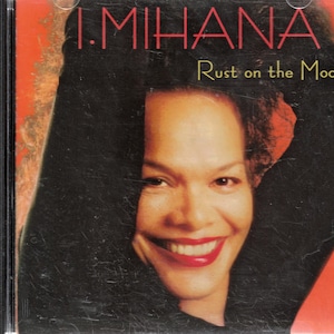 May include: CD case with a smiling woman on the cover. The woman has dark hair and red lipstick. The text "I. MIHANA" is at the top, with "Rust on the Moon" below it.