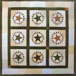 May include: A handmade quilt featuring a repeating star pattern. Each square showcases a star in varying shades of brown and green, surrounded by a sunburst design. The quilt has a dark green border and a neutral background.