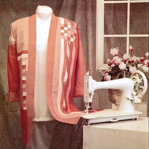 May include: A pink and white patchwork jacket with a white long-sleeved shirt underneath. A white sewing machine is on a table in the background.