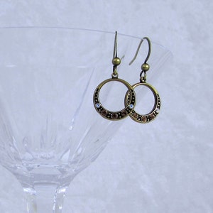 May include: A pair of gold-toned hoop earrings with a circle of brown and white rhinestones around the edge.