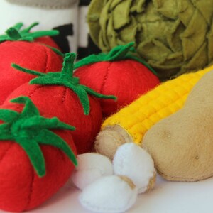 Pu&ograve; includere: Una collezione di alimenti giocattolo in feltro che include tre pomodori rosso brillante con piccioli verdi, una pannocchia di mais gialla, una patata color marrone chiaro, un carciofo verde rotondo e piccoli pezzi bianchi, realizzati in tessuto.