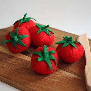 Eine Ansammlung von fünf runden, leuchtend roten Filztomaten, die jeweils mit einem aufgenähten grünen Filzstiel und Blättern versehen sind. Die Tomaten sind in einer Gruppe angeordnet und zeigen ihre weiche Textur und den Kontrast zwischen Rot und Grün.
