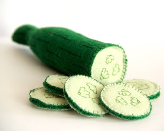 Può includere: Un cetriolo giocattolo di feltro con un esterno verde e un interno verde chiaro. Il cetriolo è tagliato in diversi pezzi, ognuno con un disegno cucito di una foglia.