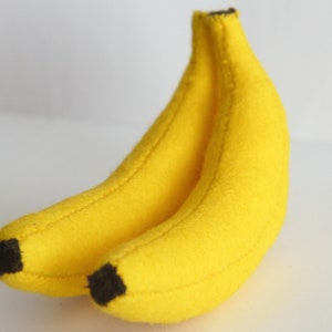 Könnte beinhalten: Zwei gelbe Filzbananen, eine auf der anderen, mit braunen Filzstielen.