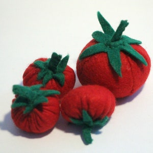 Pu&ograve; includere: Una collezione di quattro pomodori in feltro fatti a mano di varie dimensioni. Ogni pomodoro rosso rotondo presenta un gambo e una struttura a foglie in feltro verde sulla parte superiore. I morbidi giocattoli in tessuto sono raggruppati.