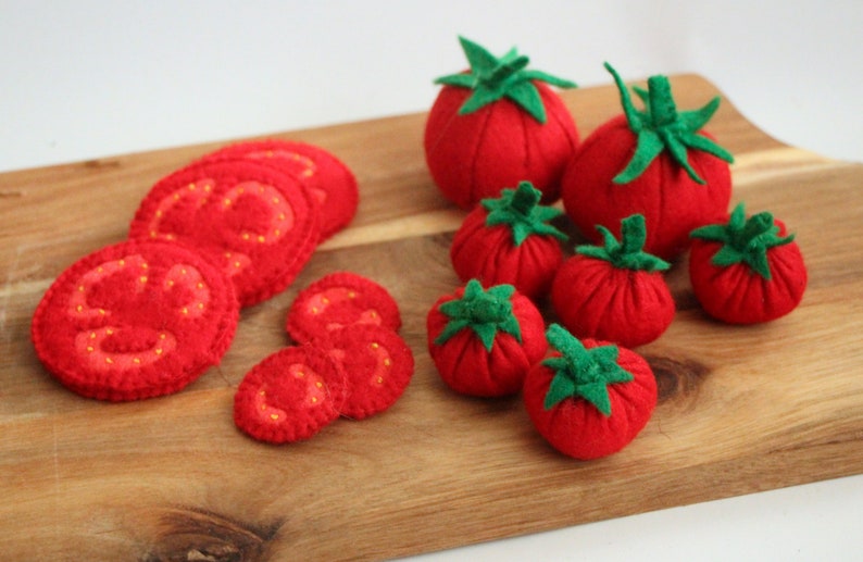 Pu&ograve; includere: Una collezione di pomodori e fette di pomodoro in feltro rosso con piccioli in feltro verde. Il set comprende diversi pomodori interi rotondi di varie dimensioni e molteplici fette piatte con dettagli cuciti in giallo.