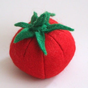 Pu&ograve; includere: Un puntaspilli in feltro rosso a forma di pomodoro, caratterizzato da una superficie testurizzata e da un picciolo in feltro verde con sei foglie appuntite sulla parte superiore. Il corpo presenta sottili rientranze verticali.
