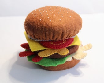 Op de afbeelding: Een hamburger speelgoed van vilt met een bruin broodje, gele kaas, rode tomaat, groene sla en een bruin patty.