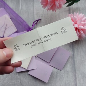 May include: A white card with the text "Take time to do what makes your soul happy." and a small black and white illustration of a birthday cake with candles. The card is folded in half and is sitting on a purple and white background.