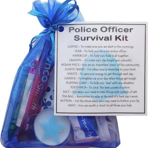 Puede incluir: Una bolsa de malla azul llena de un kit de supervivencia para agentes de polic&iacute;a. El kit incluye una estrella, un clip, un cray&oacute;n, una pieza de rompecabezas, una banda el&aacute;stica, dulces, una vela, una carta de juego, un palillo de dientes, sal, una bolsita de t&eacute;, un bot&oacute;n y una menta. La bolsa tiene una tarjeta adjunta con el texto "Police Officer Survival Kit" y una lista de art&iacute;culos con sus usos correspondientes.